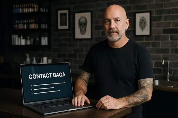 Body art practitioner seated beside a laptop displaying an online support page